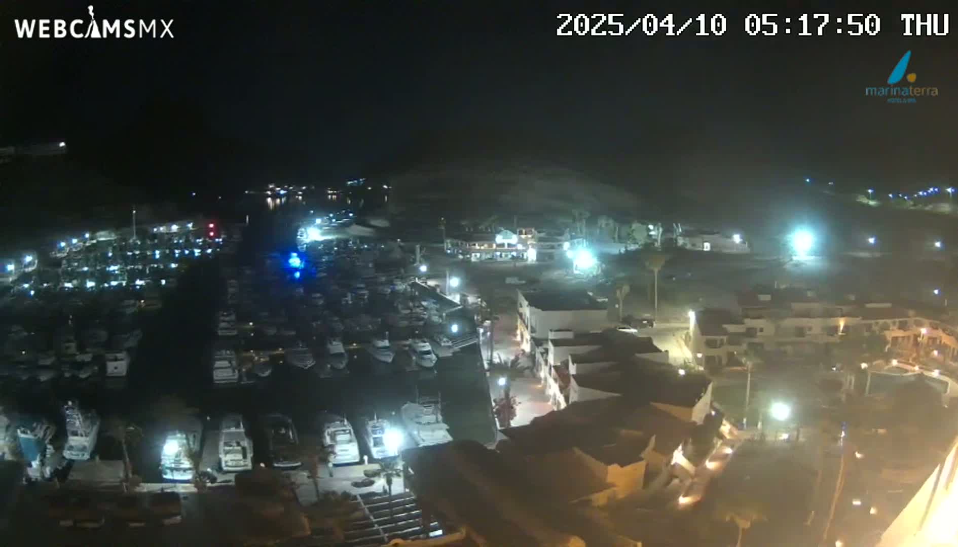 A nighttime aerial view of a marina filled with boats, adjacent to a town with illuminated buildings under a clear sky.