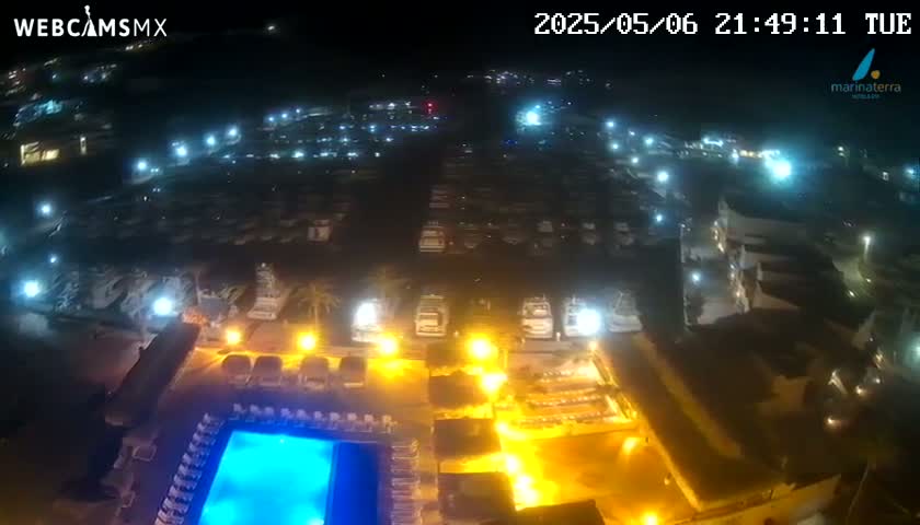 An illuminated marina at night, with a pool and surrounding buildings visible, under clear skies.