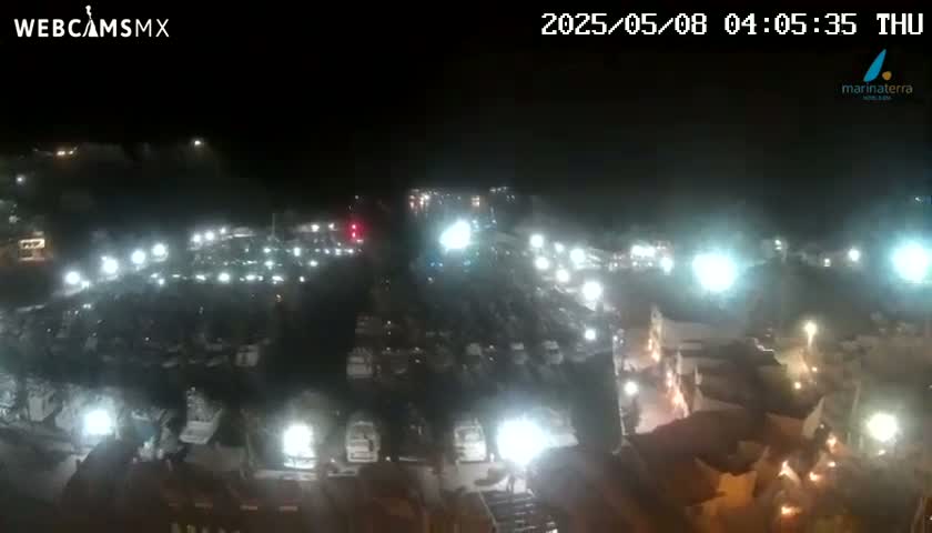 A nighttime, high-angle view of a large parking lot filled with numerous vehicles illuminated by bright lights.