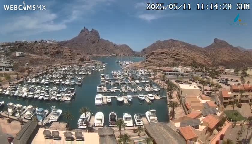A sunny day reveals a marina filled with numerous boats nestled between arid, rocky mountains.