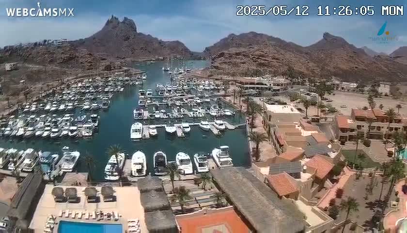 A marina filled with boats is nestled between arid, rocky mountains under a clear, sunny sky.