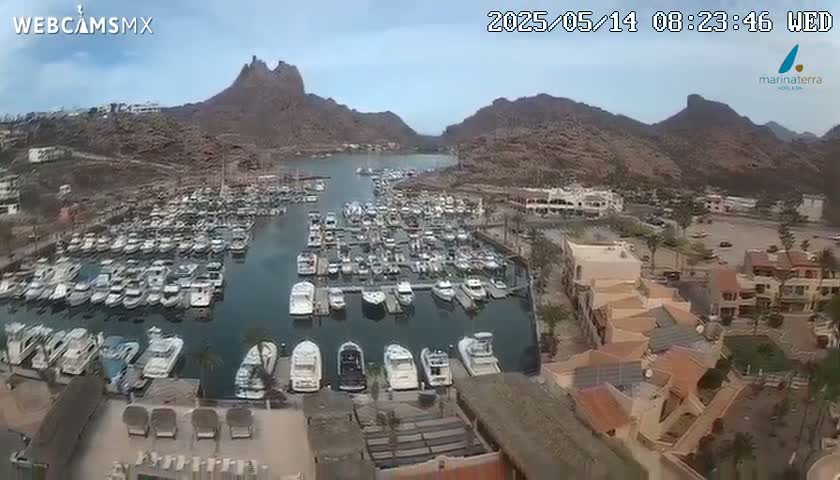 A marina filled with numerous boats is nestled between rocky mountains under a mostly clear sky.