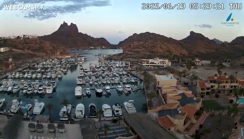 A marina filled with numerous boats is nestled between rocky hills under a twilight sky.
