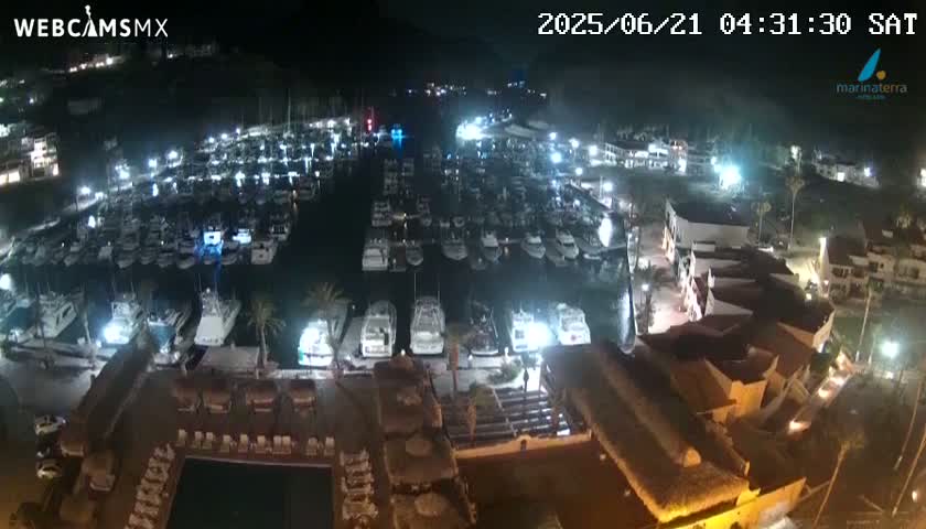 A nighttime aerial view shows a marina filled with boats and surrounding buildings under clear skies.