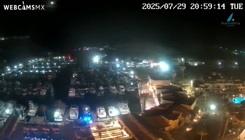 A nighttime aerial view of a marina filled with boats, adjacent to a brightly lit complex of buildings.