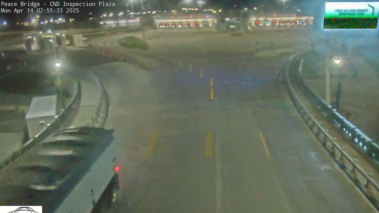 A nighttime, overhead view shows an empty highway intersection near a building with some vehicles in the distance under hazy conditions.