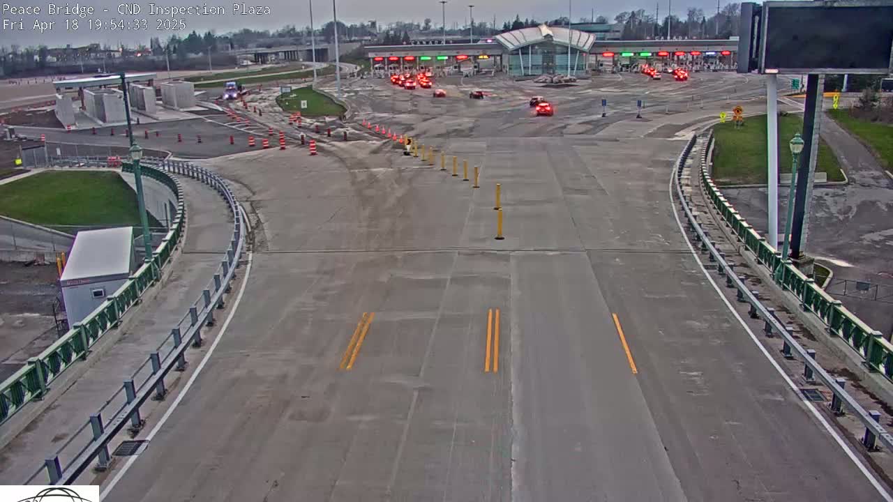 A roadway curves toward a border inspection plaza with several vehicles waiting under an overcast sky.