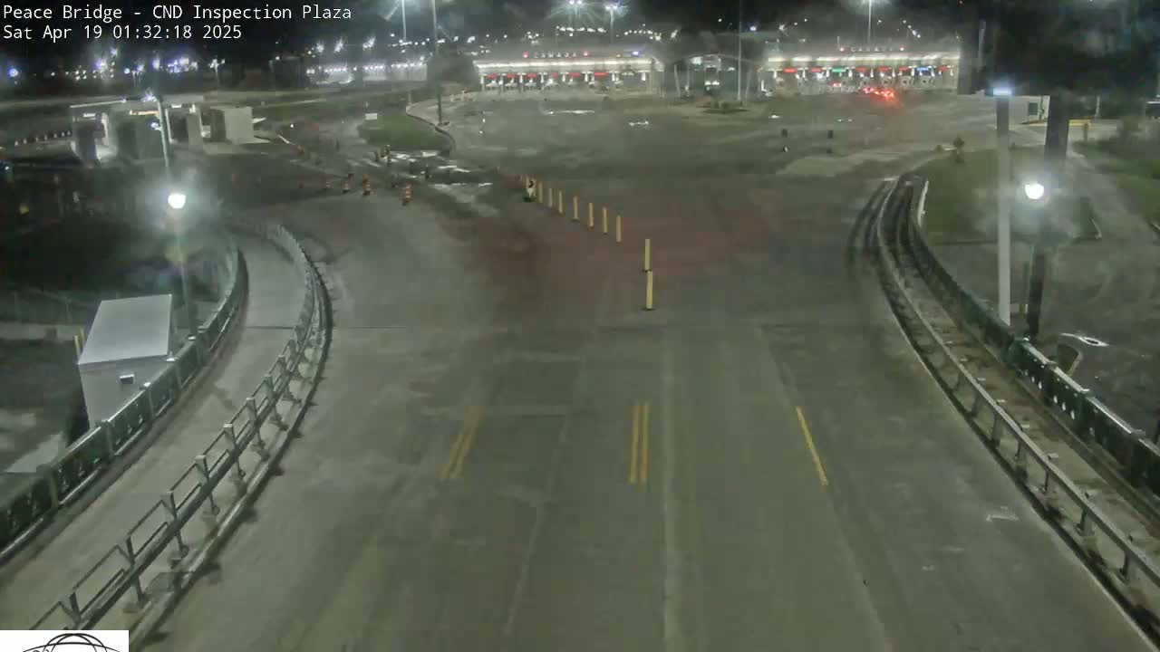 A nighttime overhead view of a mostly empty border crossing inspection plaza with a roadway curving towards the inspection booths.