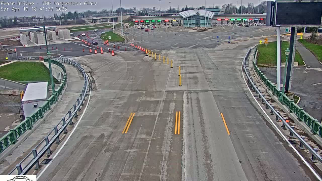 A wide, mostly empty roadway curves toward a border inspection plaza under an overcast sky.