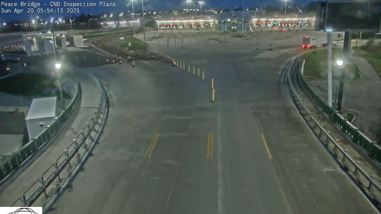 A mostly empty, dimly lit highway intersection at night, with a border inspection plaza visible in the background.