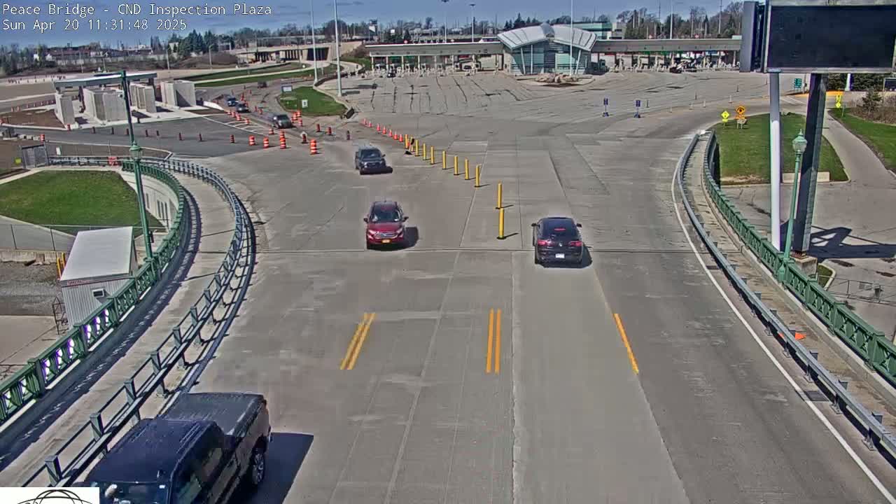 A sunny day at a border crossing inspection plaza shows several vehicles navigating a roadway and approaching inspection booths.