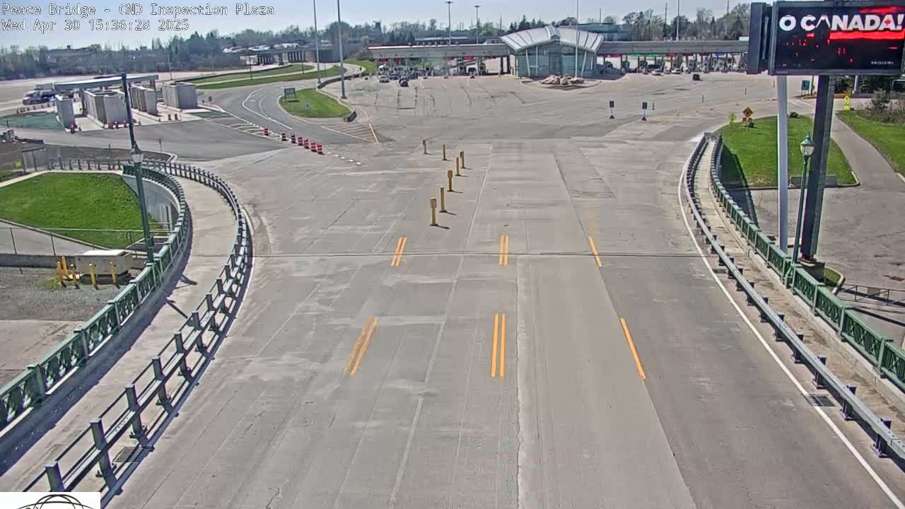 A mostly empty roadway curves toward a border crossing inspection plaza on a sunny day.