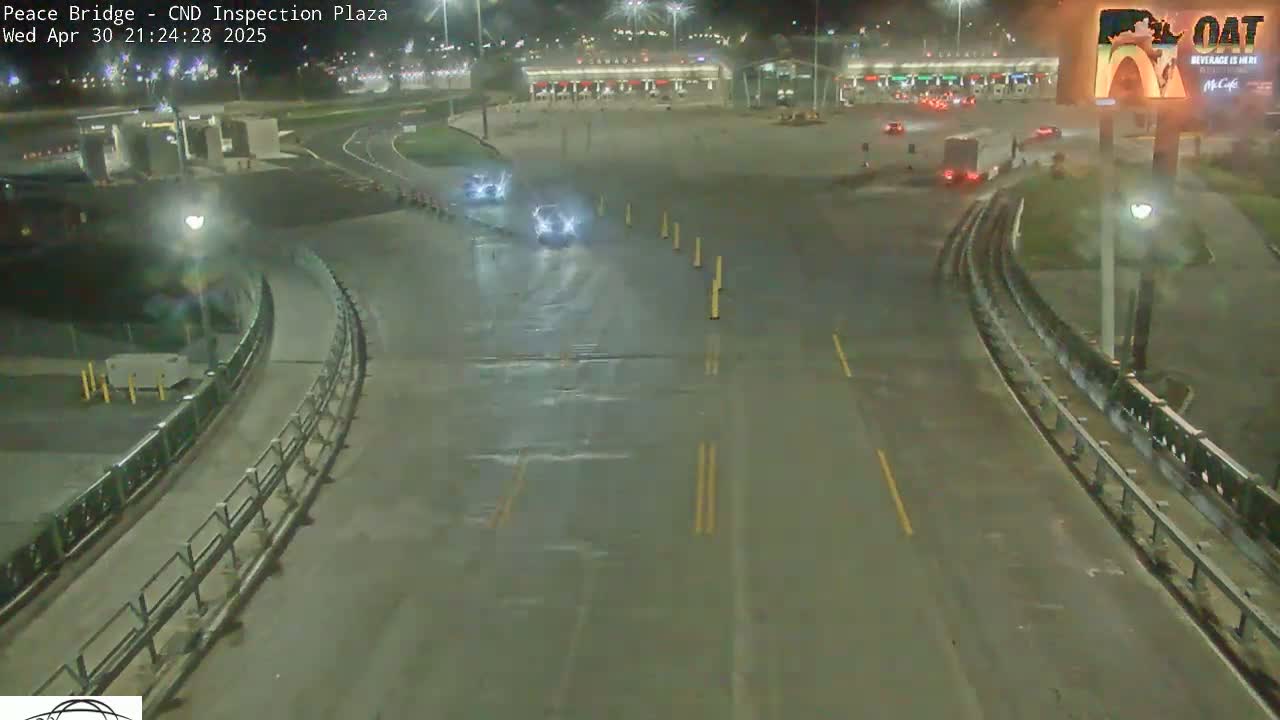 A wet, nighttime view of a highway curving through a border inspection plaza with a few vehicles visible.