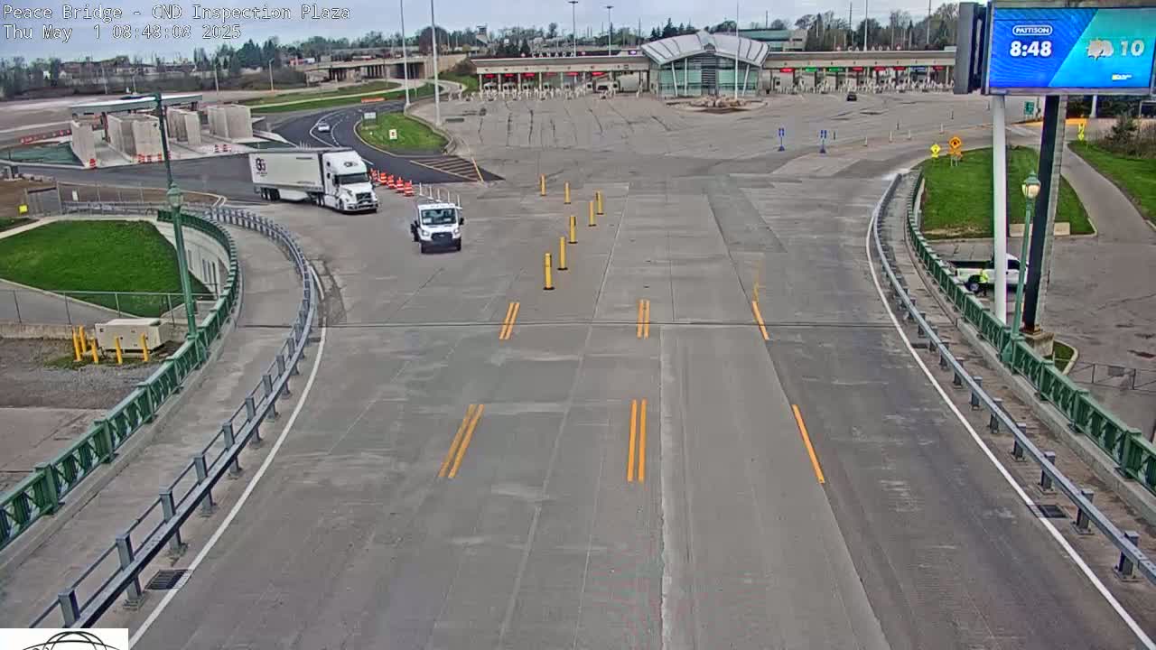 A mostly empty roadway curves toward a border inspection plaza under a partly cloudy sky.