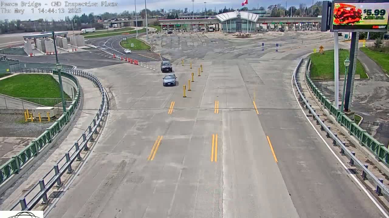 A mostly empty highway approaches a border inspection plaza under a partly sunny sky.