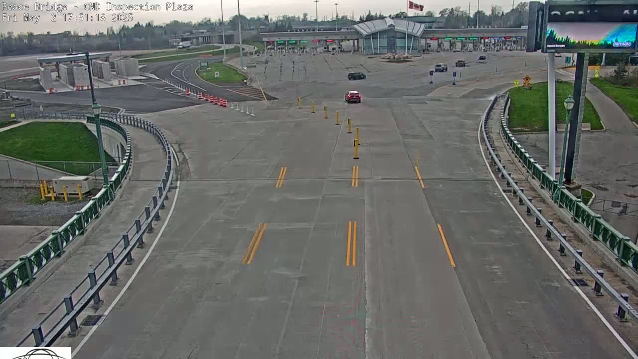 An empty roadway curves toward a border crossing inspection plaza under an overcast sky.