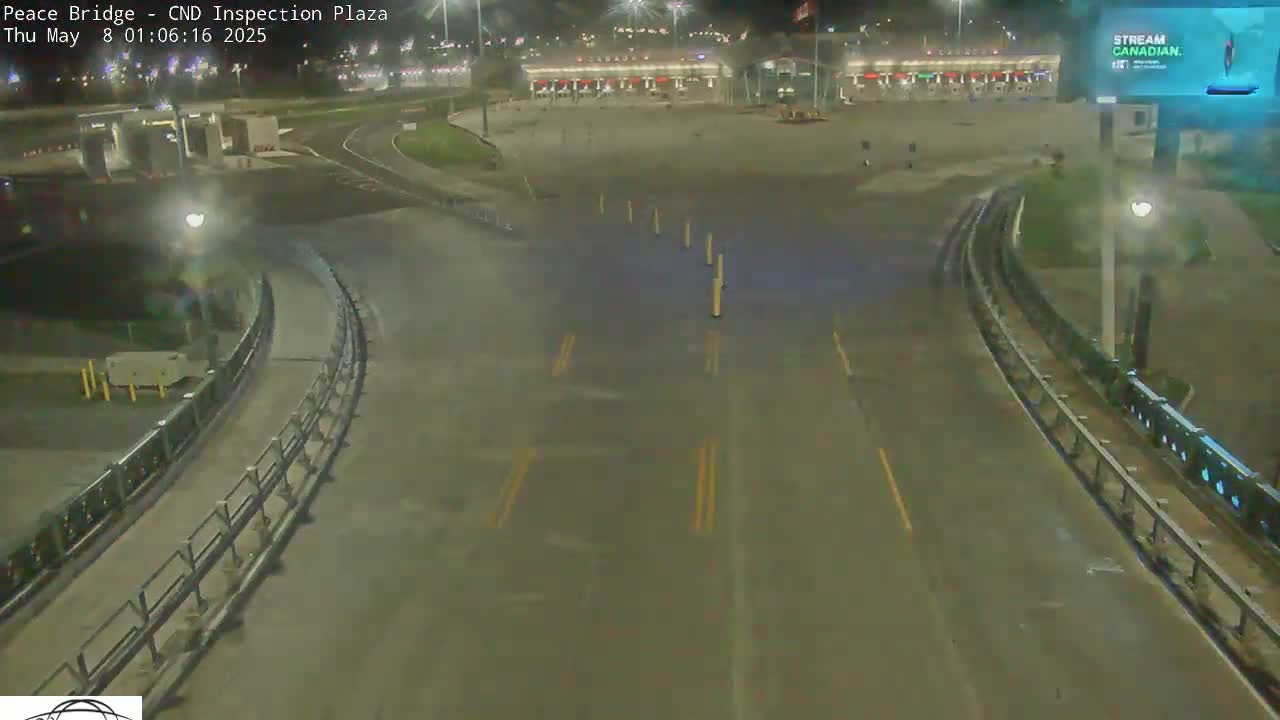 A nighttime view of a mostly empty highway inspection plaza with curving roadways and bright lights.