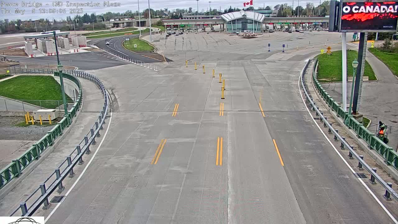 An empty roadway curves toward a border crossing plaza on a partly cloudy day.