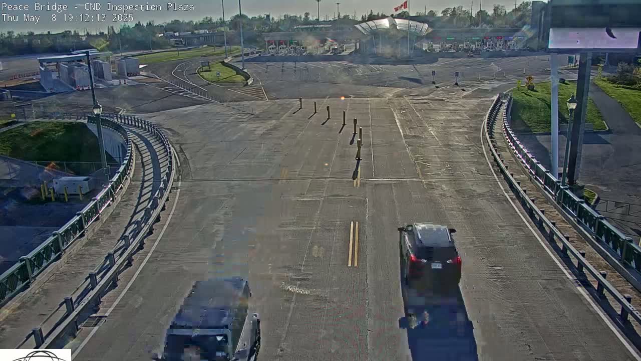 Two vehicles approach a border inspection plaza on a sunny day.