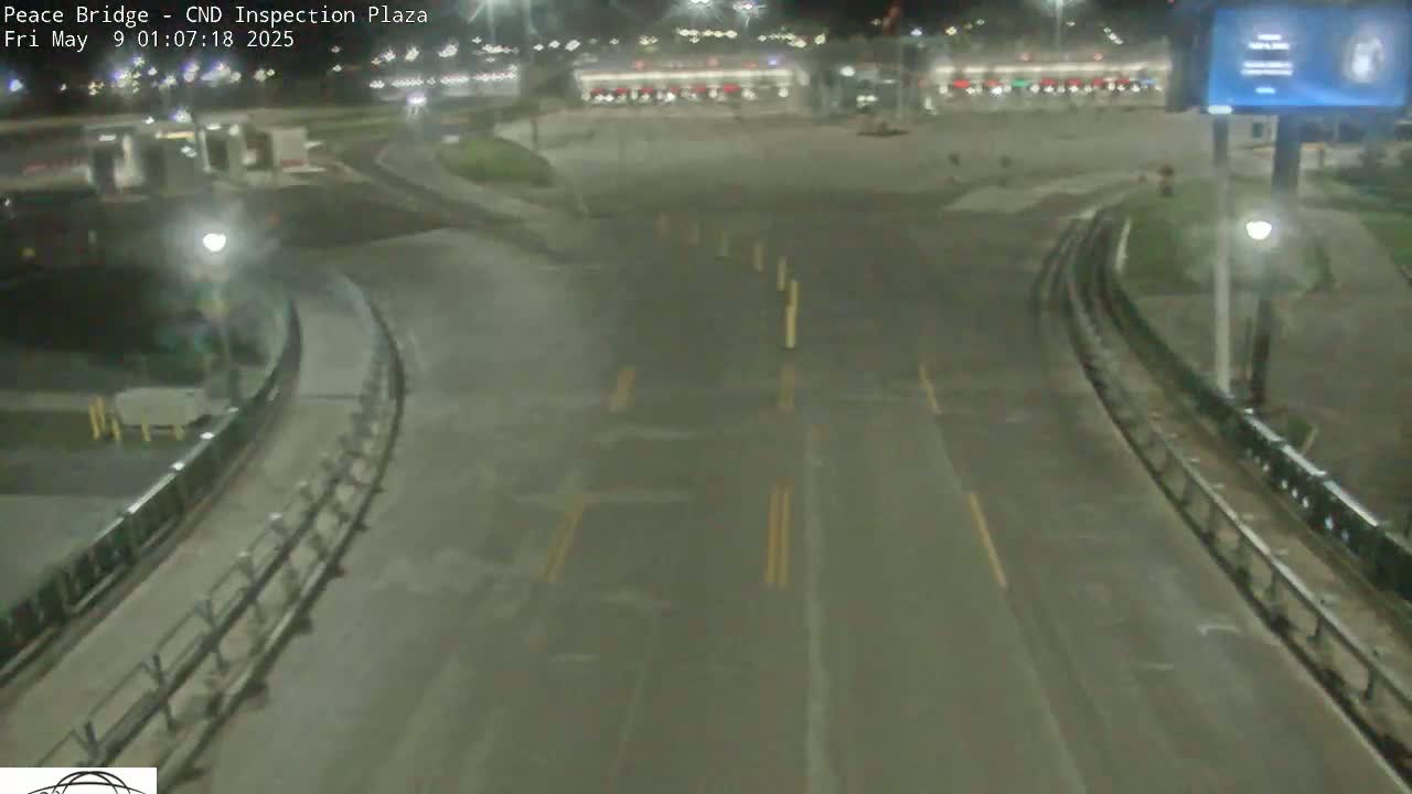 A nighttime, wet road curves through an empty inspection plaza with lights illuminating the scene.