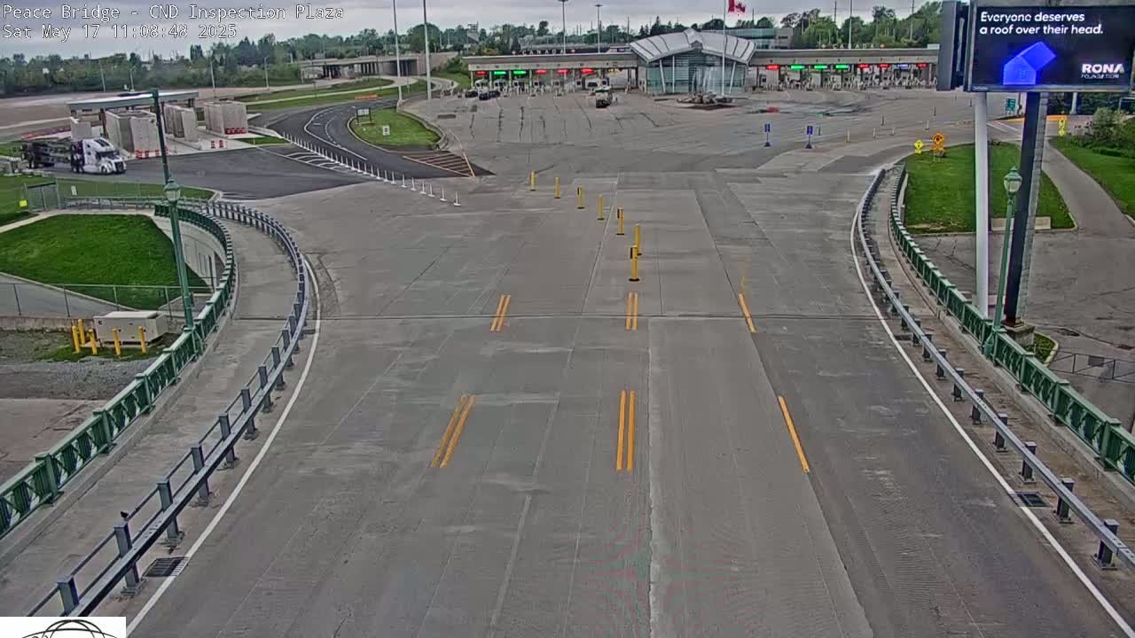 A mostly empty roadway curves toward a border inspection plaza under an overcast sky.