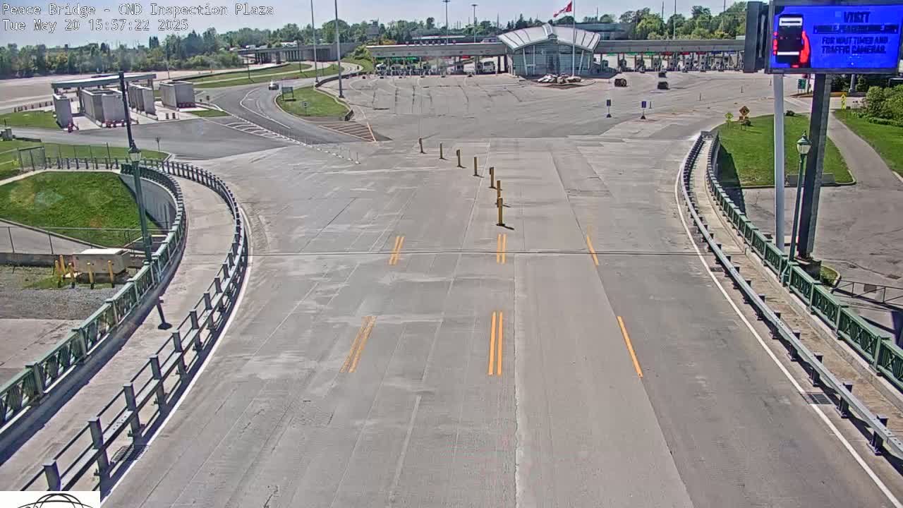 A mostly empty roadway curves toward a border inspection plaza on a sunny day.