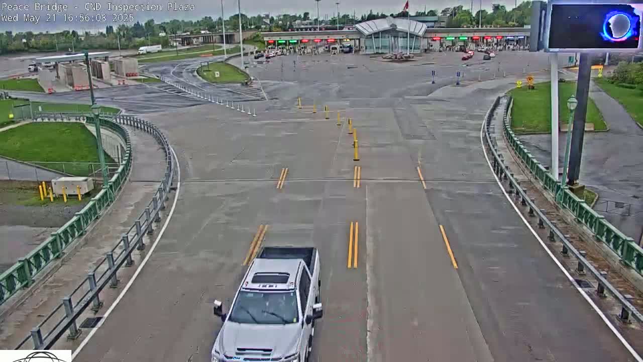 A white pickup truck approaches a border inspection plaza on a wet, overcast day.