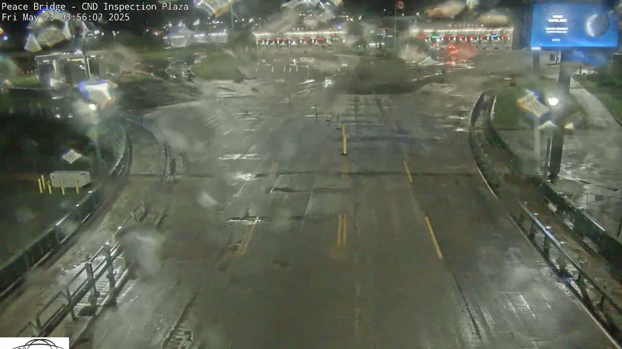 A wet, empty roadway at night curves through a border inspection plaza.