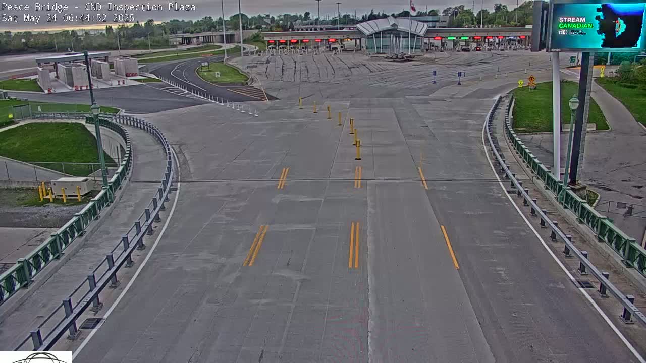 An empty roadway curves toward a border inspection plaza under overcast skies.
