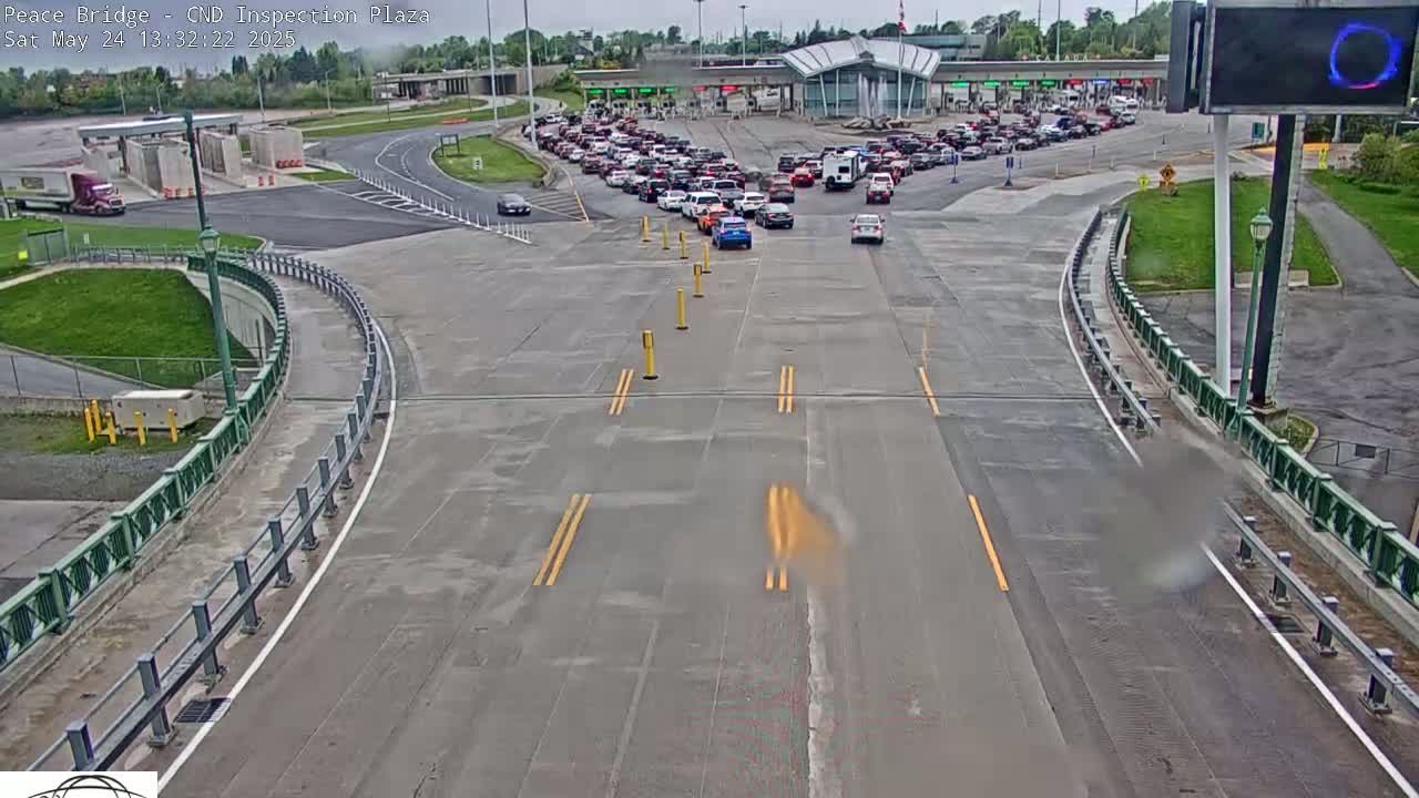 A long line of vehicles is waiting at a border crossing inspection plaza on a partly cloudy day.