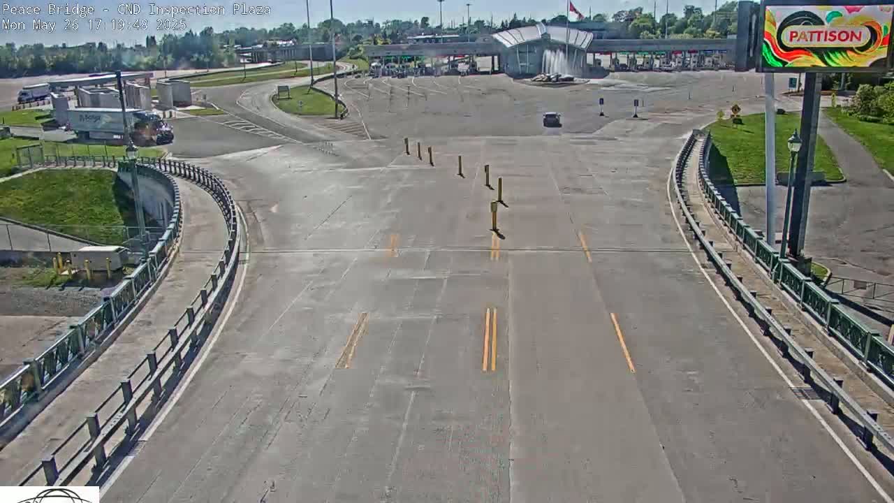 A mostly empty highway approaches a border inspection plaza on a sunny day.