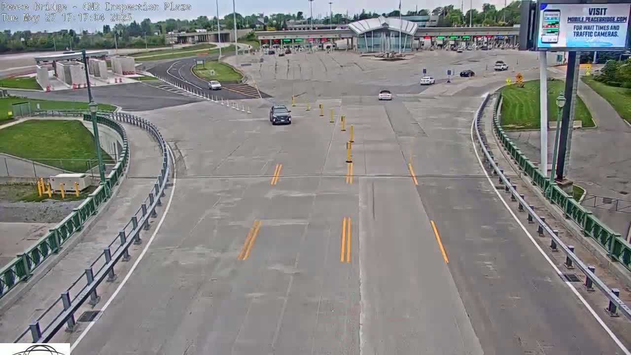 A mostly empty highway curves toward a border crossing inspection plaza under a partly cloudy sky.