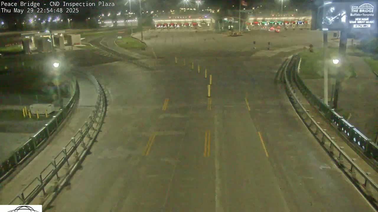 A nighttime, mostly empty roadway curves through a border inspection plaza.