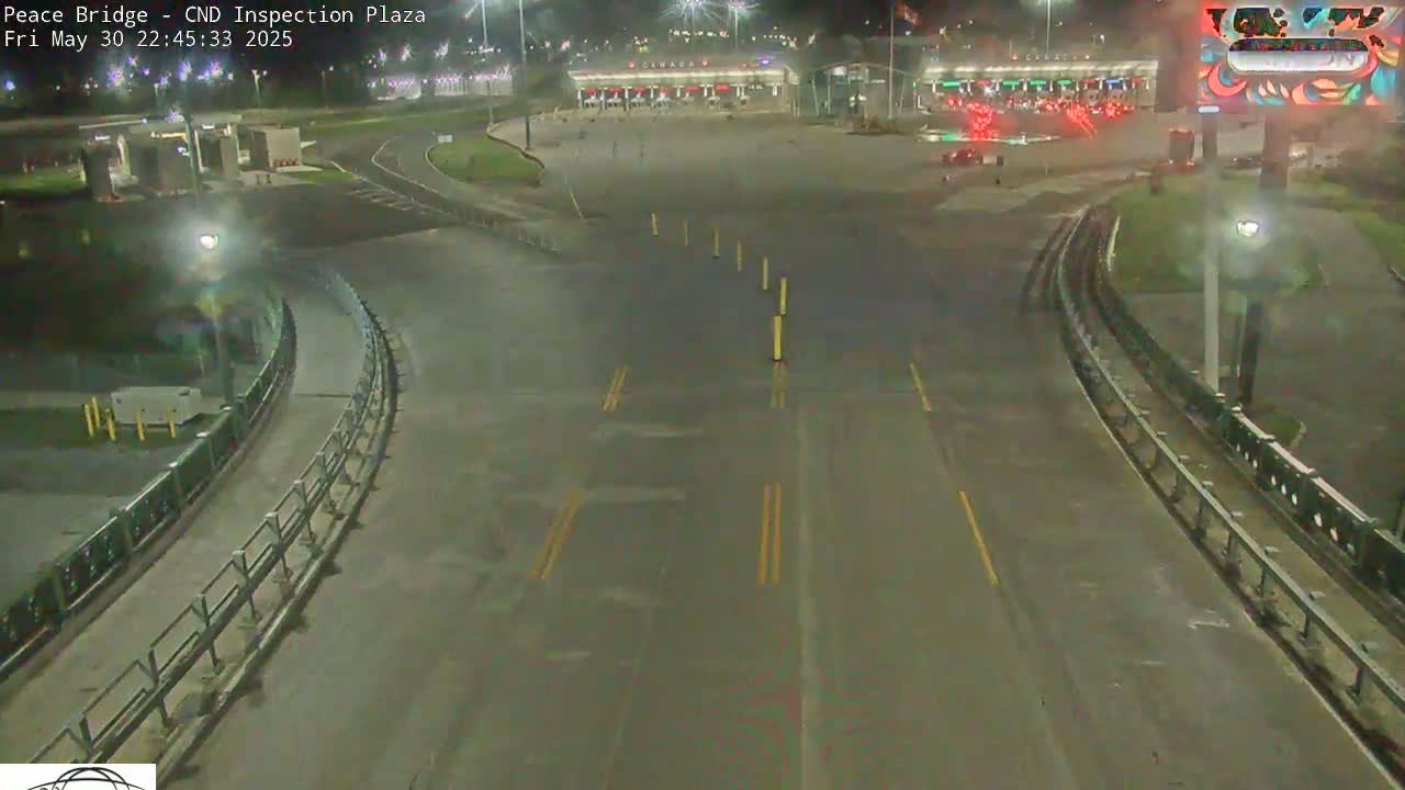 A nighttime overhead view of a mostly empty border crossing inspection plaza with a few vehicles present and wet pavement.
