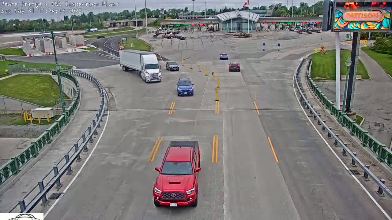 A mostly empty border crossing plaza on a partly cloudy day, with several cars and a semi-truck visible.