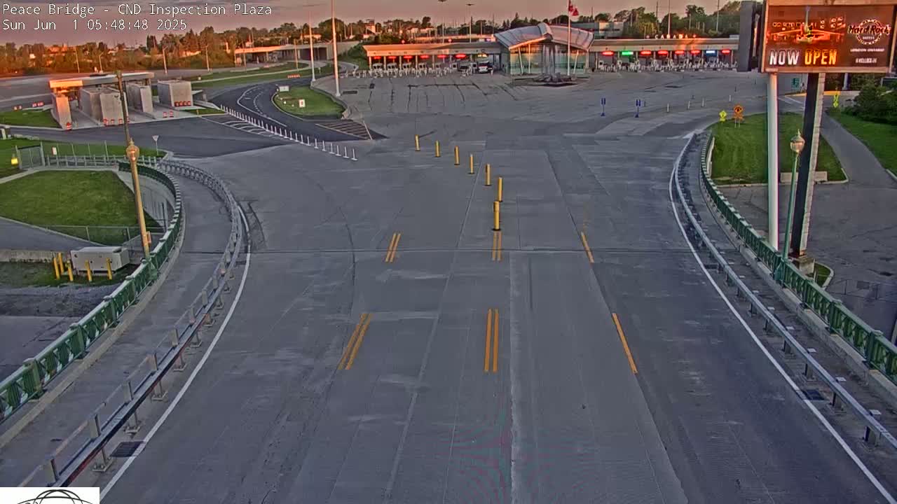 An empty highway curves toward a border inspection plaza under a clear, twilight sky.