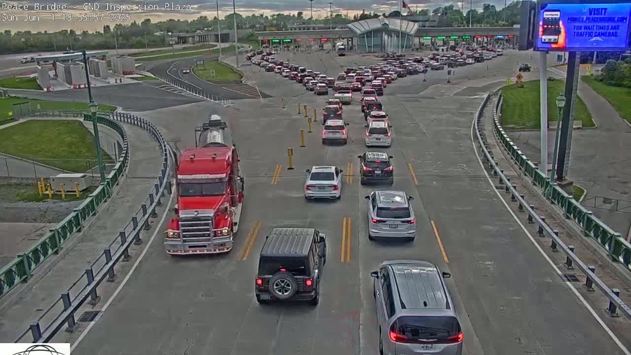 A long line of vehicles waits at a border crossing under partly cloudy evening skies.
