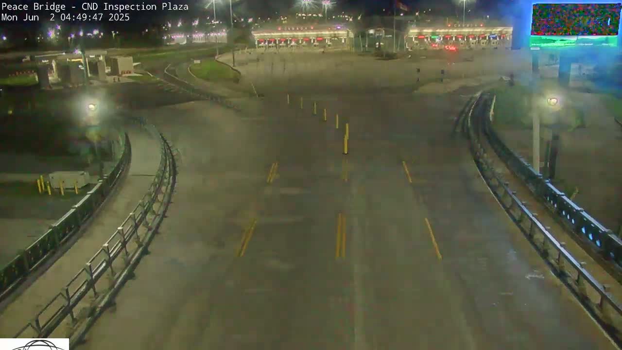 A wet, nighttime view of a mostly empty border inspection plaza with curving roadways and several tall light poles.
