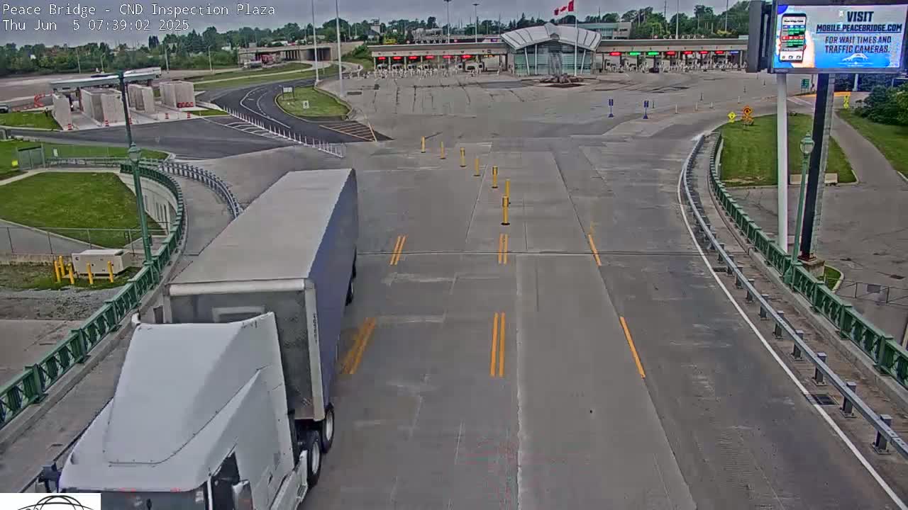 A large white semi-truck approaches a border inspection plaza on an overcast day.