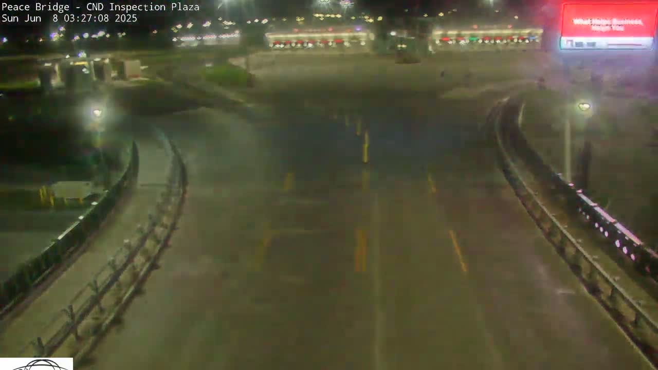 A wet, empty roadway curves through a nighttime border inspection plaza.
