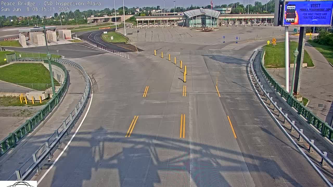 An empty roadway curves toward a border inspection plaza on a sunny day.