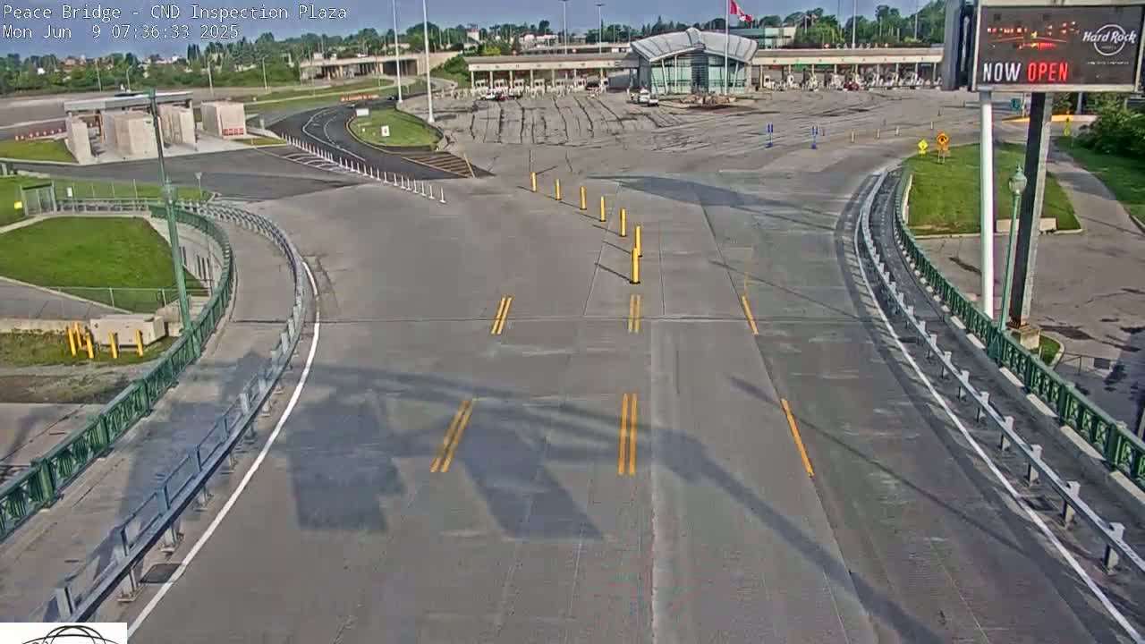 A sunny, mostly empty border crossing inspection plaza with roadways leading to and from a modern building.
