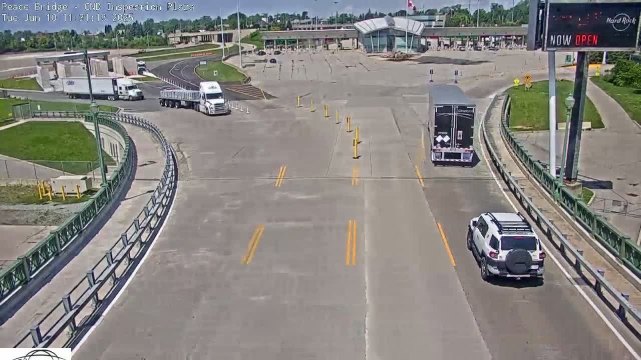 A sunny outdoor view of a border inspection plaza with several vehicles, including trucks and an SUV, driving on the roads.