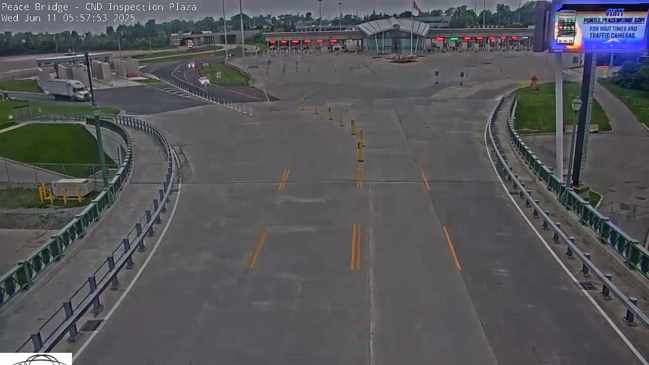 An empty border inspection plaza with a large paved area and roadways, under overcast daytime conditions.