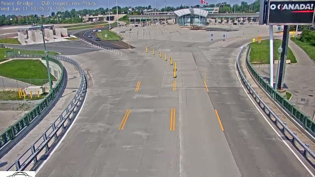 A roadway curves toward a border inspection plaza under a sunny sky.