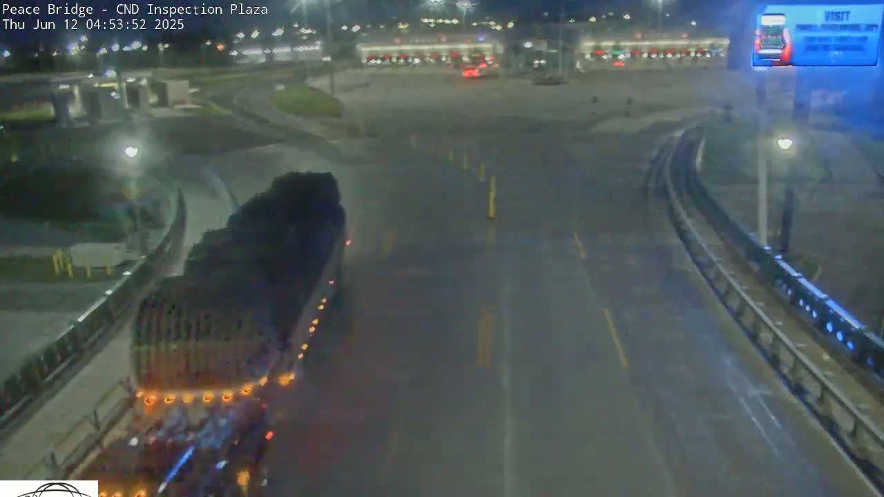 A large truck drives on a wet road at night toward a mostly empty inspection plaza.