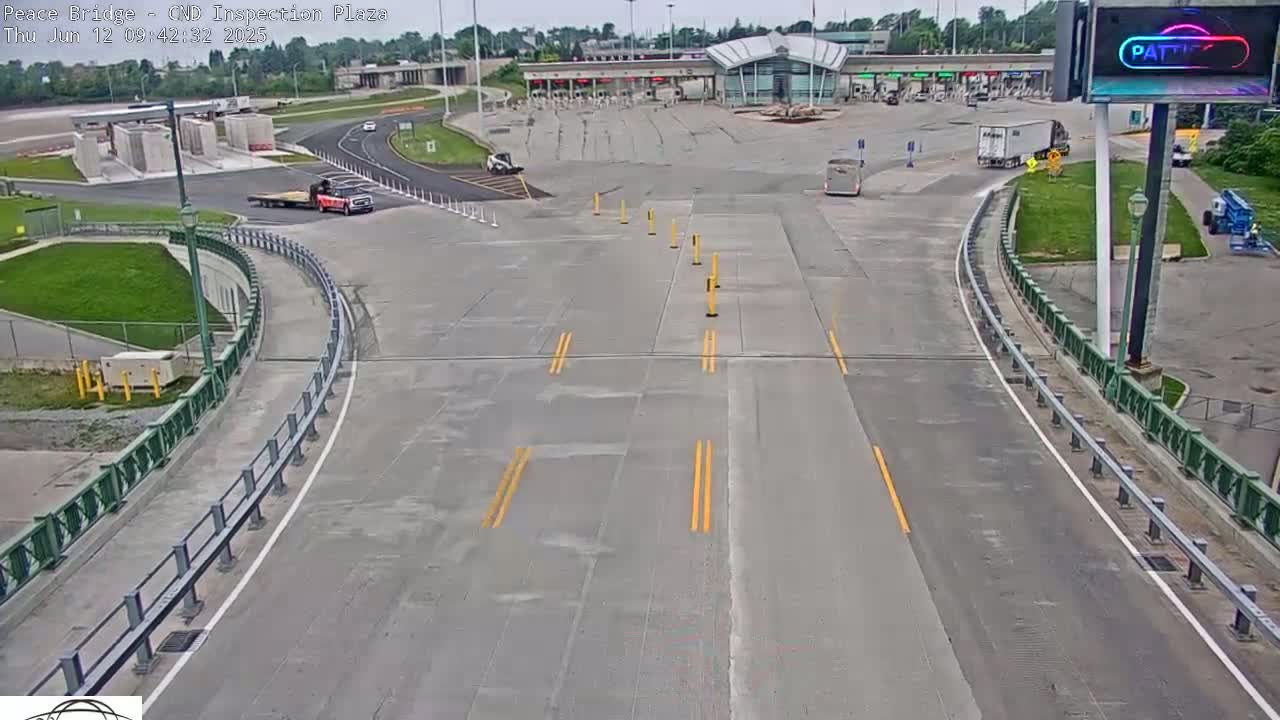 A mostly empty border inspection plaza on a partly cloudy day, with a few vehicles visible and a road curving towards the inspection booths.