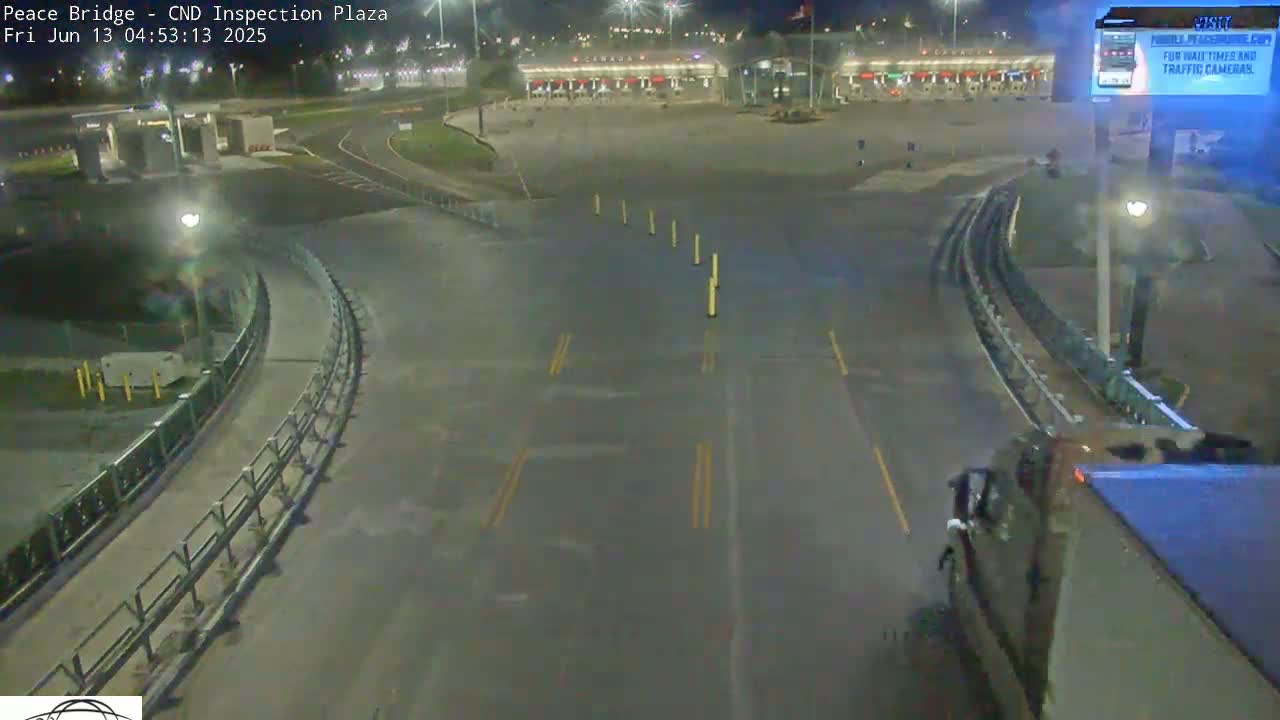 A nighttime view of an empty border inspection plaza with a curved roadway leading to it, under dark conditions.