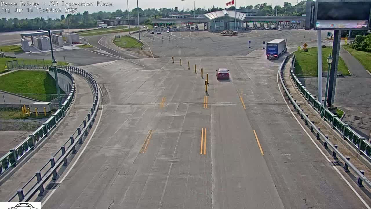 A mostly empty highway curves toward a border inspection plaza under a sunny sky.