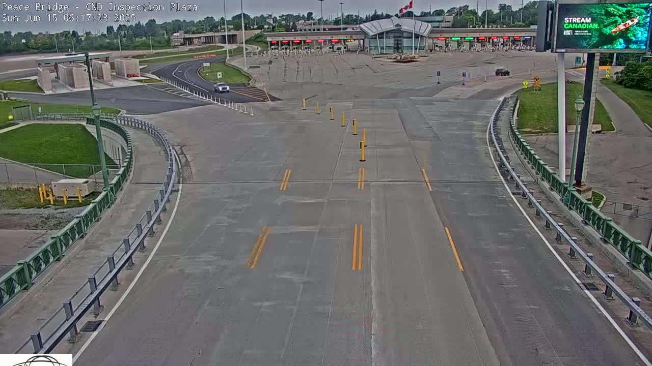 An empty roadway curves toward a border crossing station under an overcast sky.